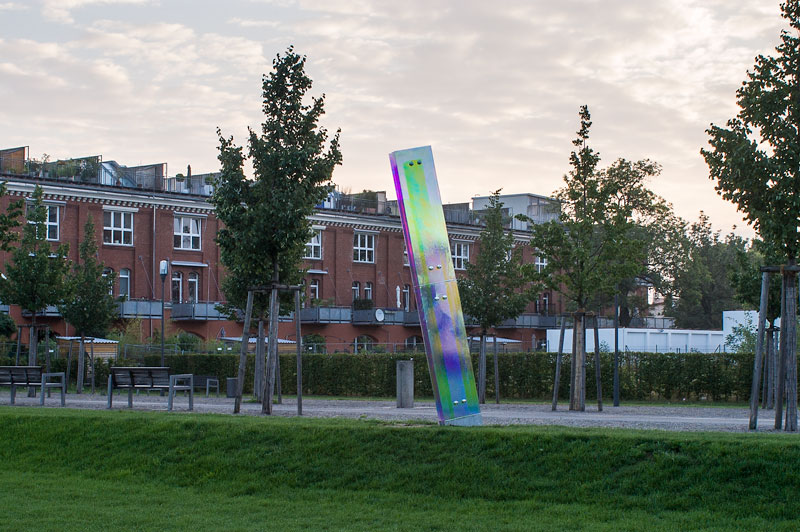 Schrägstehende Glasstele vor saniertem Altbau