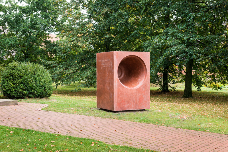 Rote Betonskulptur vor Bämen